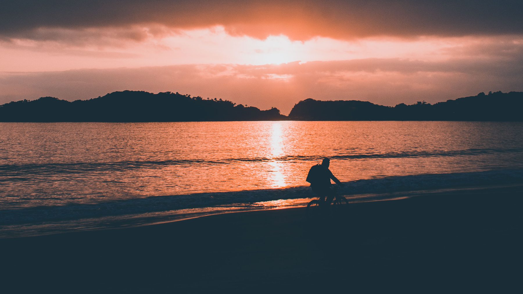 Silhouetted cyclist riding along the shore at sunset